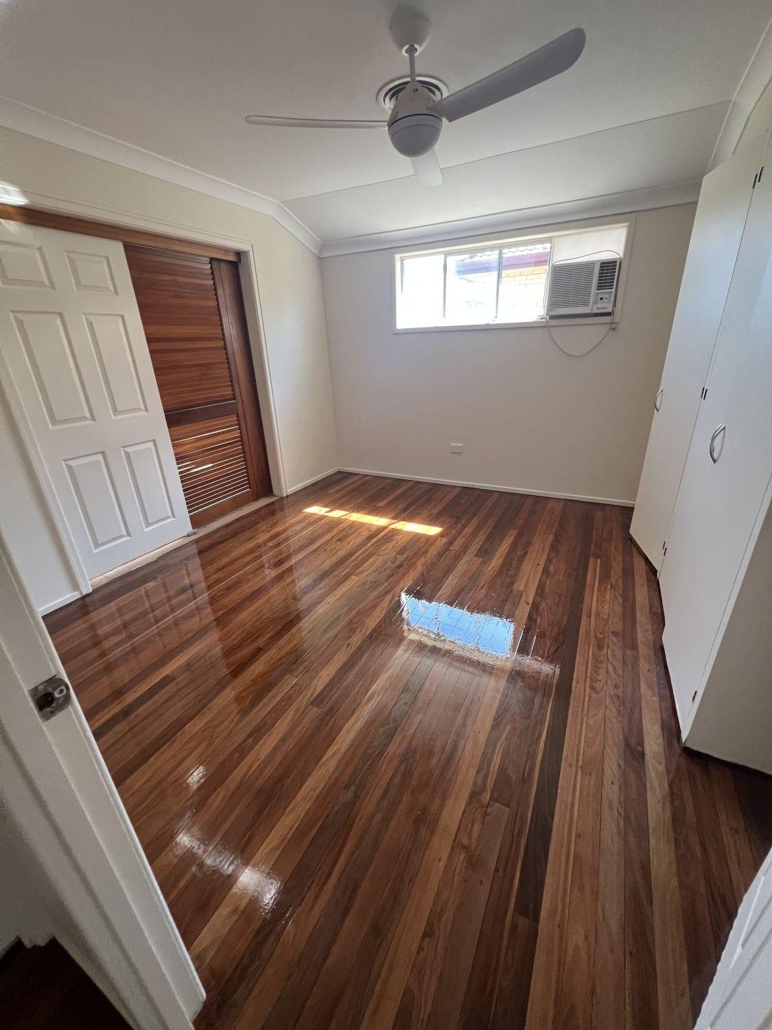 Empty room with polished wood floor, white walls, window air conditioner, ceiling fan, and closet with white doors.