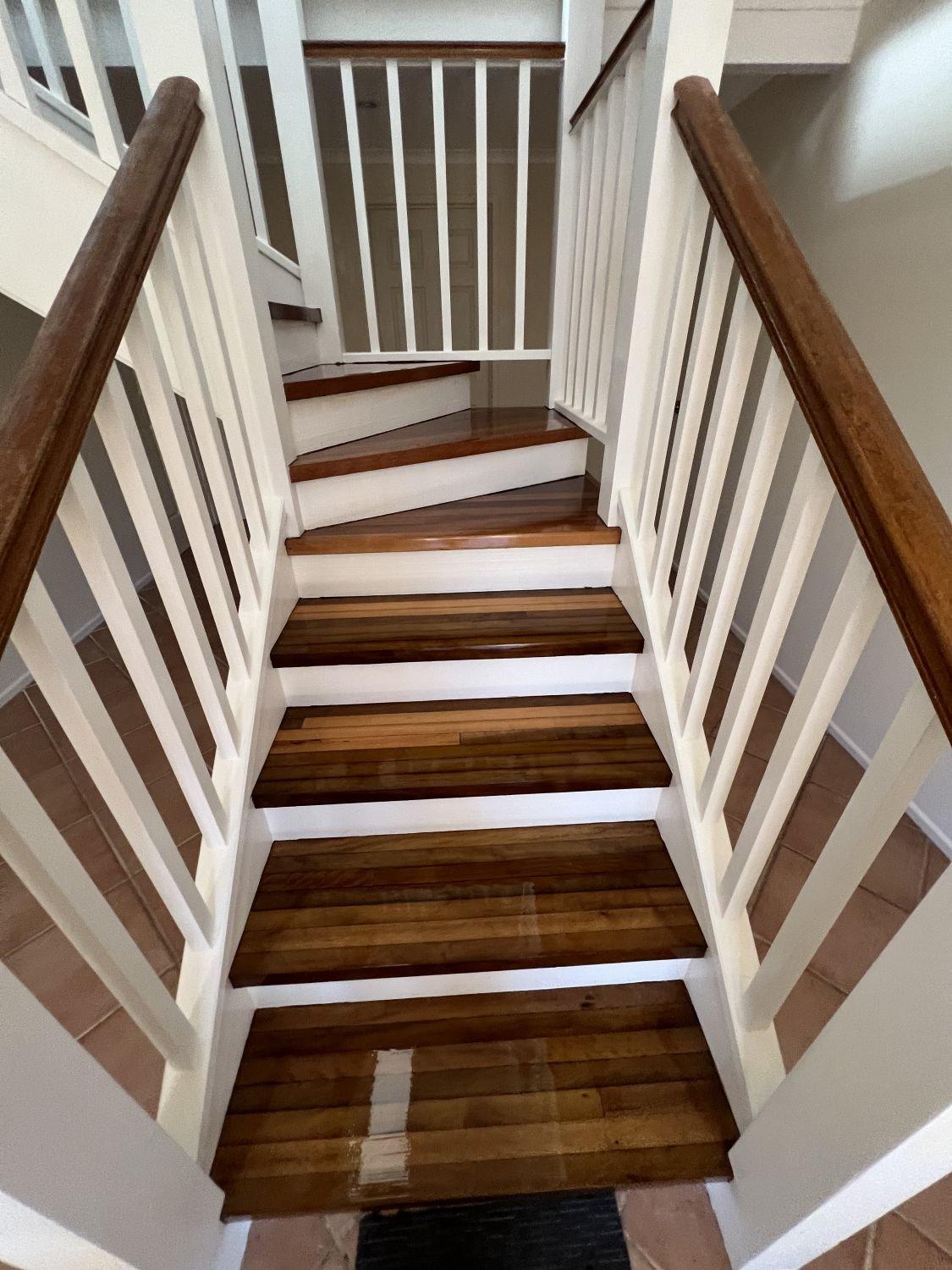 View of a staircase with wooden steps, white risers, white railings, and brown handrails.