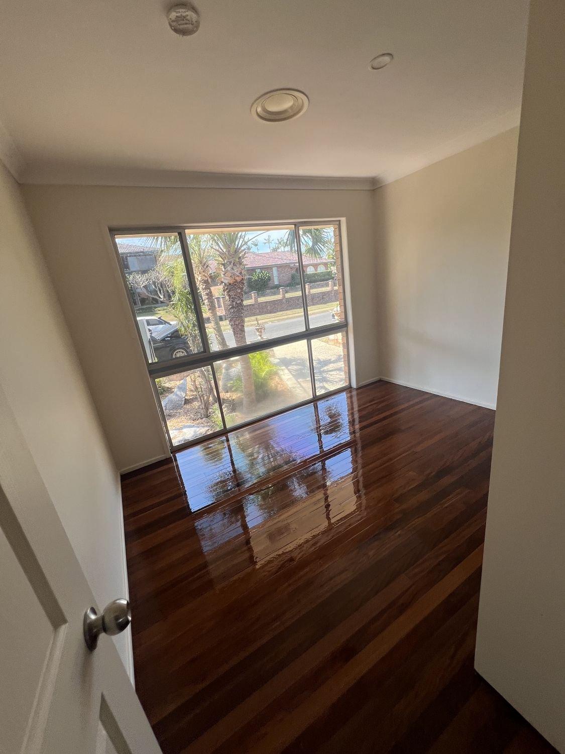 Empty room with polished hardwood floors, white walls, and a large window.