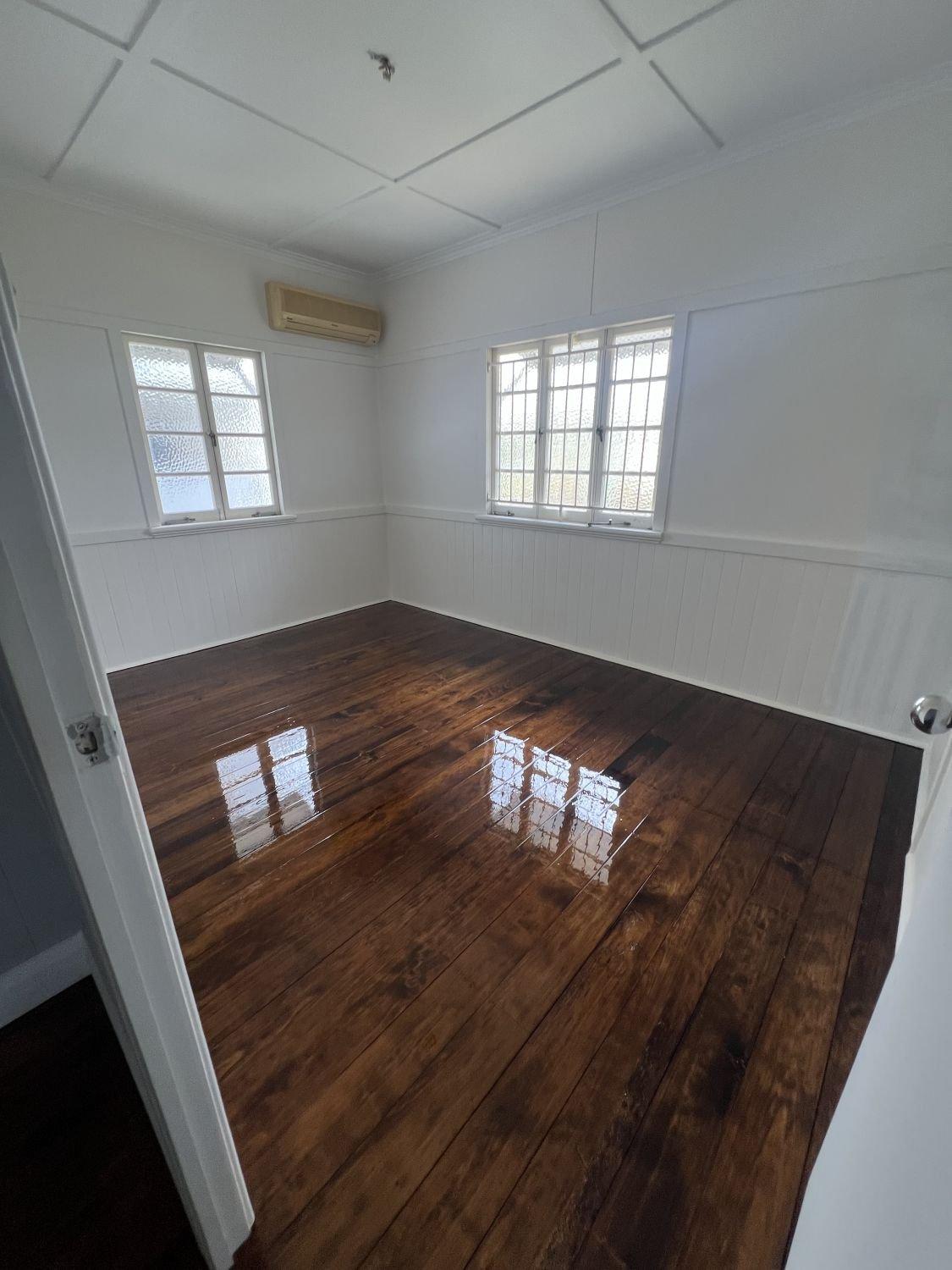 Empty room with white walls, wood panelling, polished wooden floors and two windows.
