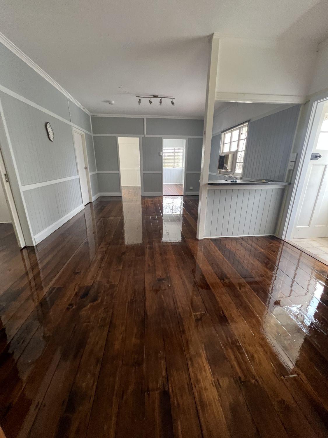 Living room with polished hardwood floors, light grey panelled walls and doorways to other rooms.