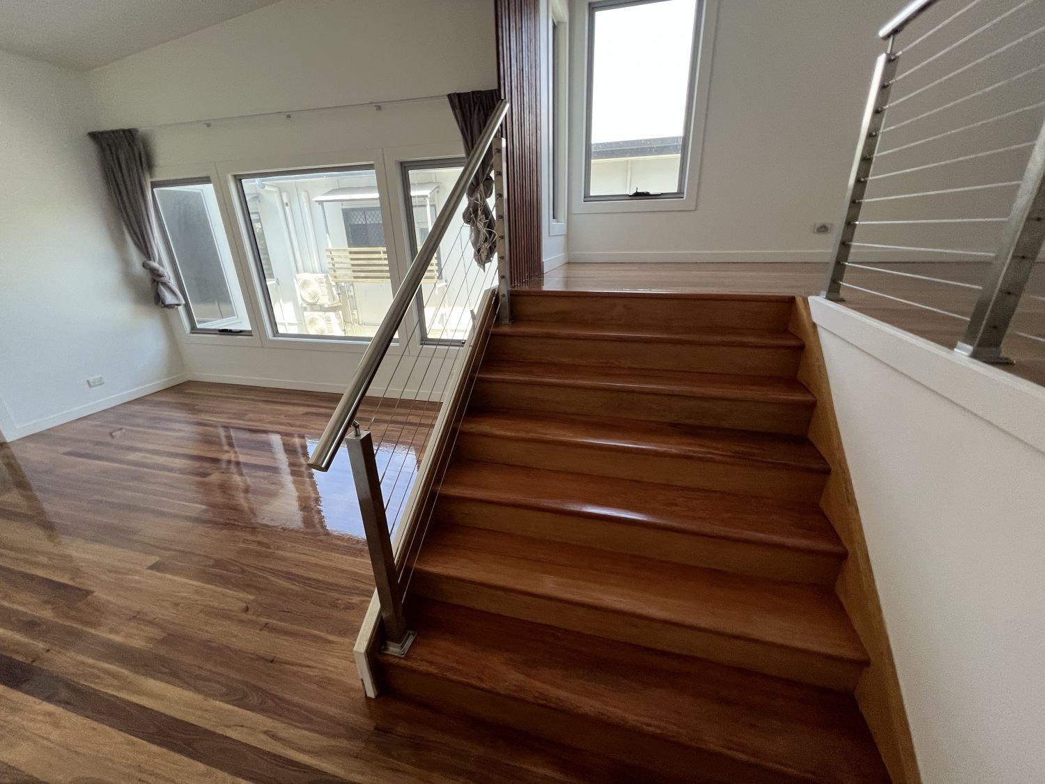 Interior view of a room with hardwood floors, stairs with wooden treads, and large windows with curtains.