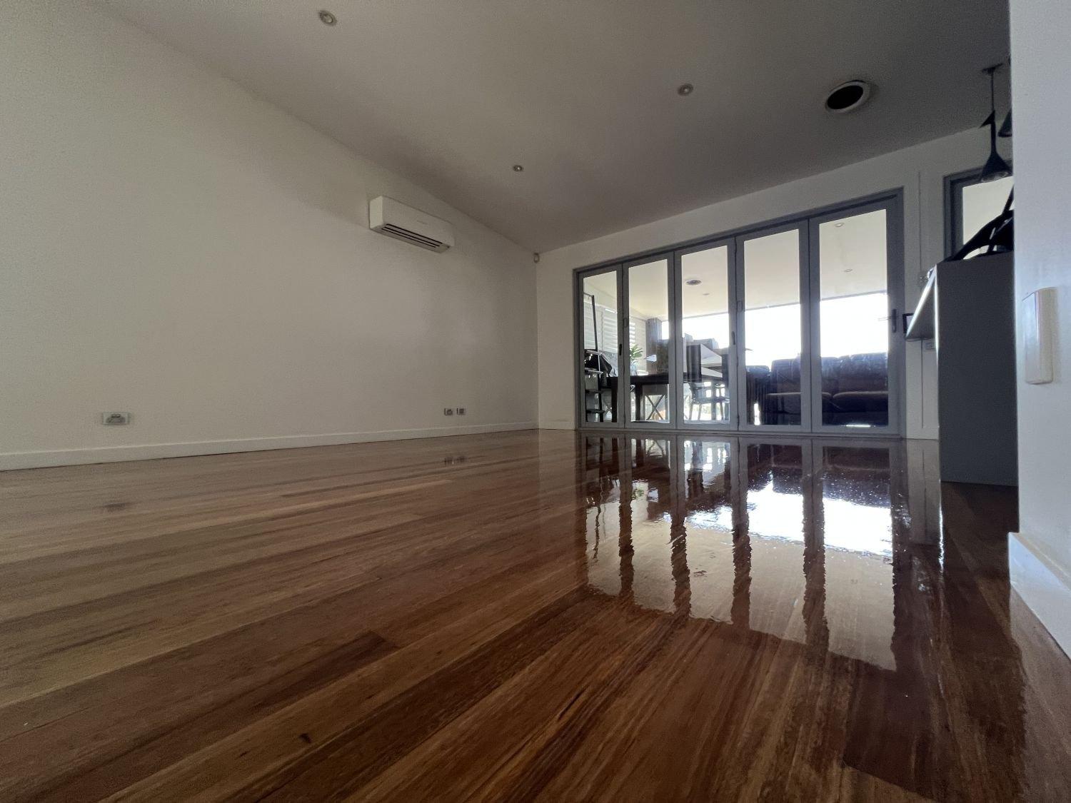 Living room with wooden floor, glass doors opening to a balcony and wall-mounted air conditioning.