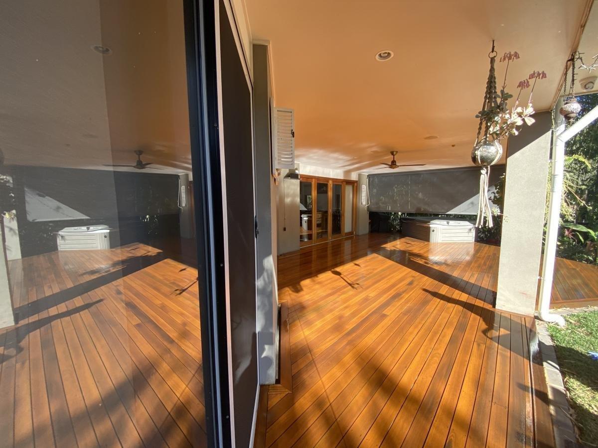 Spacious outdoor patio with polished wooden floors, hanging plants, and ceiling fans.