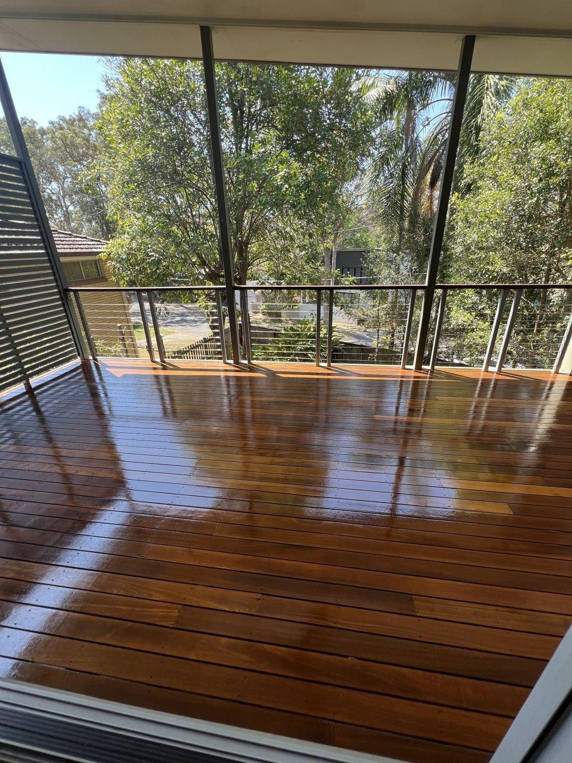 Wooden balcony with glass railing overlooking a leafy suburban neighbourhood.