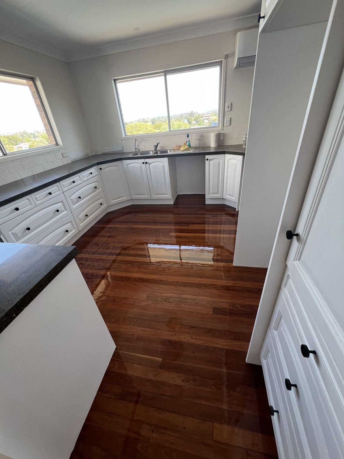 Kitchen with white cabinets, black countertops, polished wooden floors and large windows.