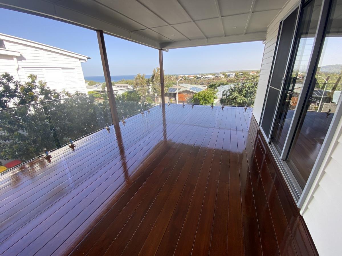 Balcony with polished wooden flooring, glass railing and an ocean view.
