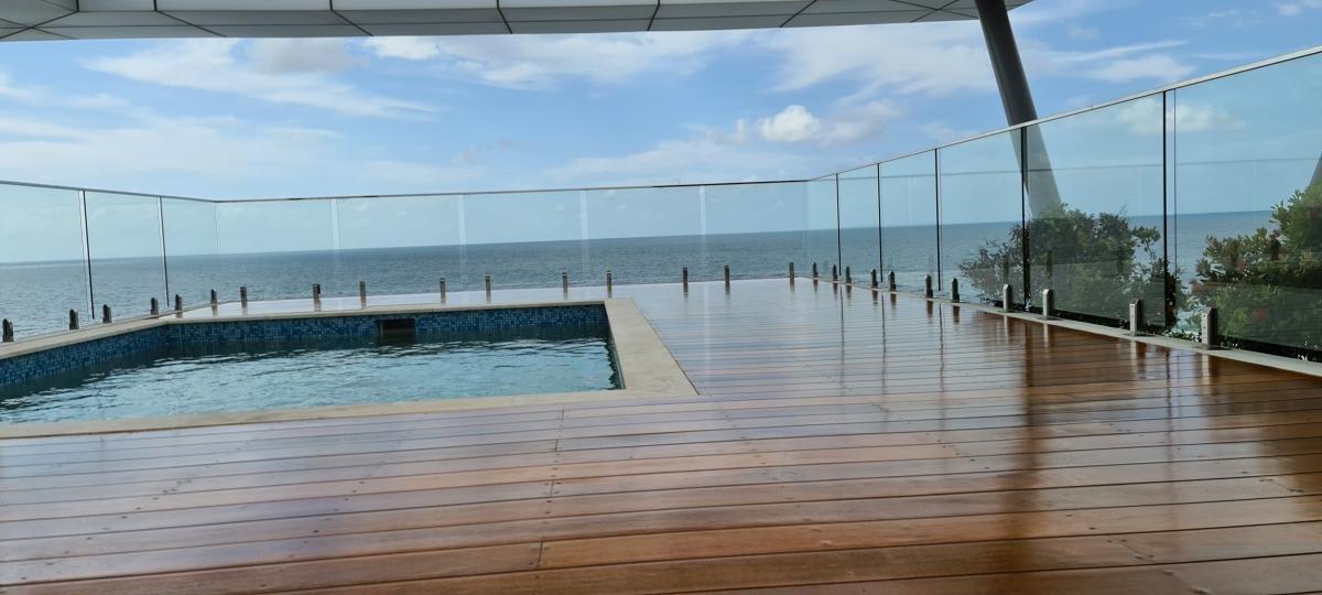 Ocean view from a rooftop deck with a hot tub, timber flooring and glass railing.