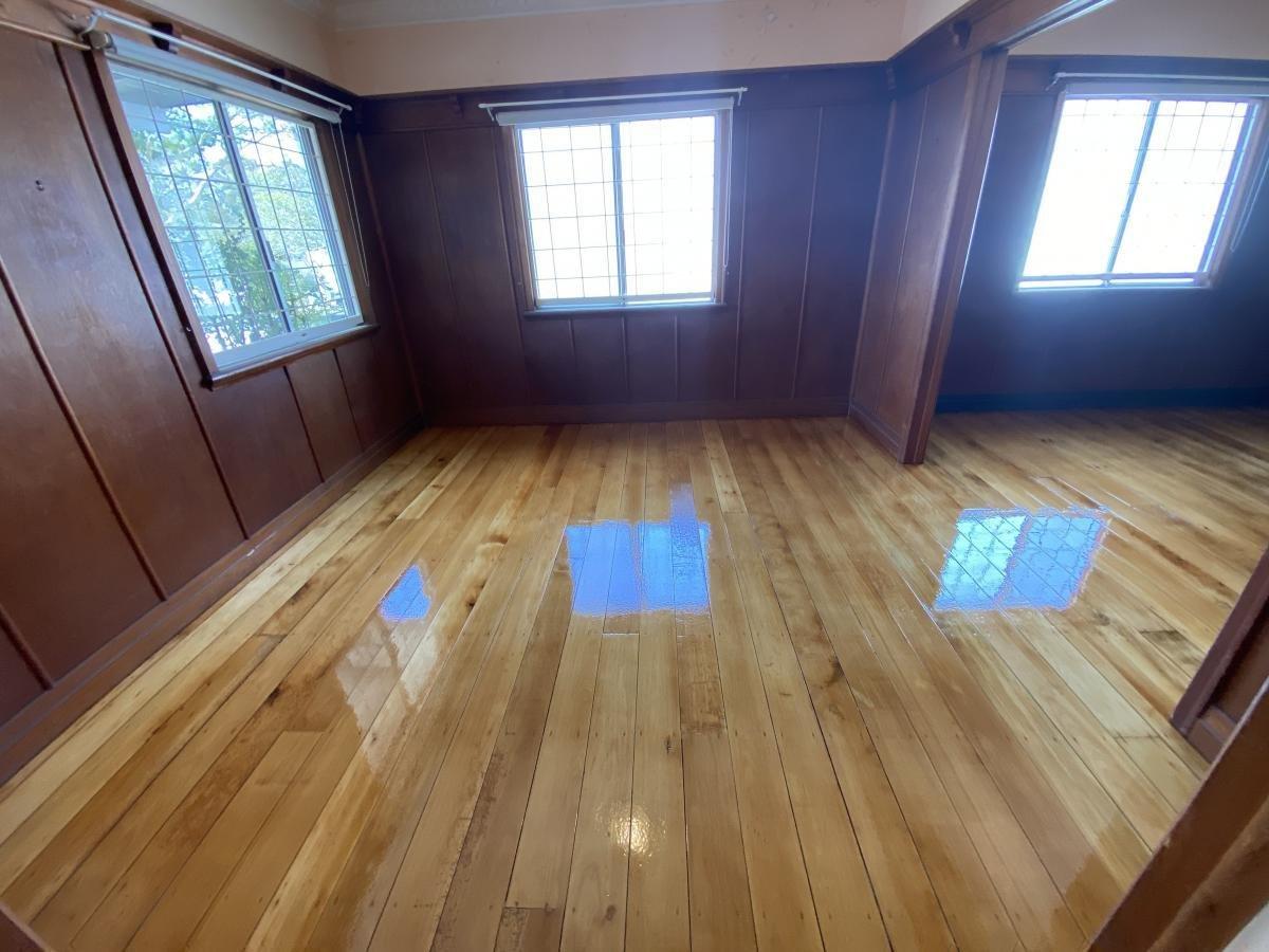 Room with shiny hardwood floor, grid-patterned windows and dark timber wall panelling.