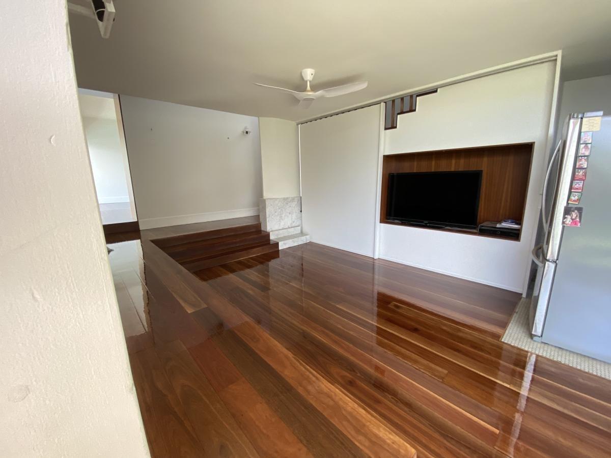Living room with polished wooden floors, ceiling fan and wall-mounted television.