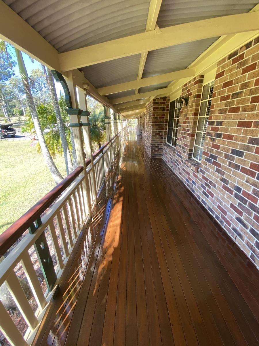 Long wooden porch with beige railing and brick wall.